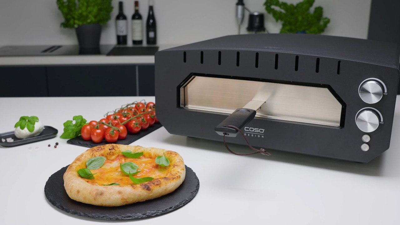Pizza oven with pizza, tomatoes, basil and ingredients on the table.