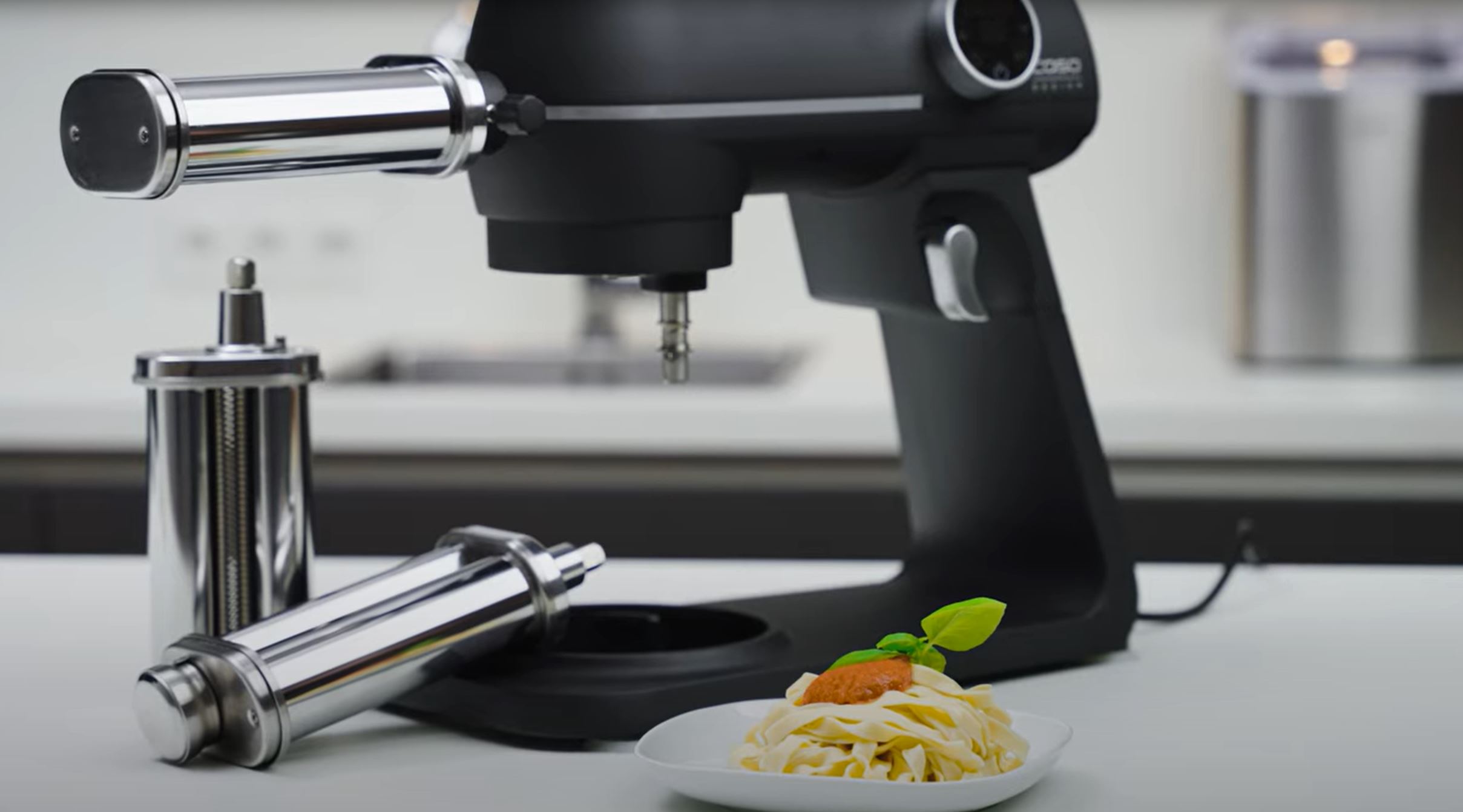 Kitchen machine with pasta attachment and finished pasta on a plate