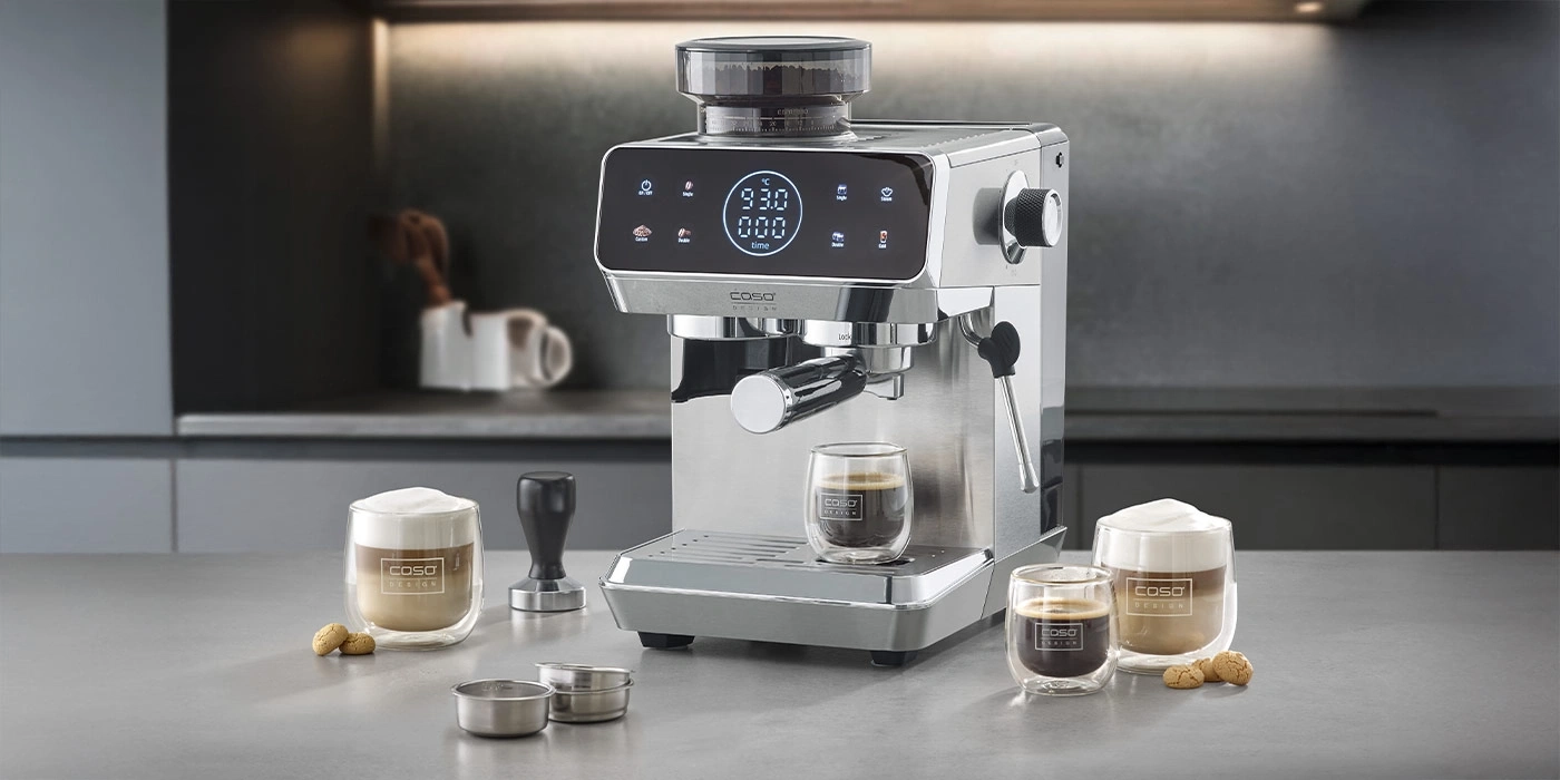 Eine Espressomaschine mit drei Gläsern Kaffee und Gebäck auf einer Arbeitsplatte.
