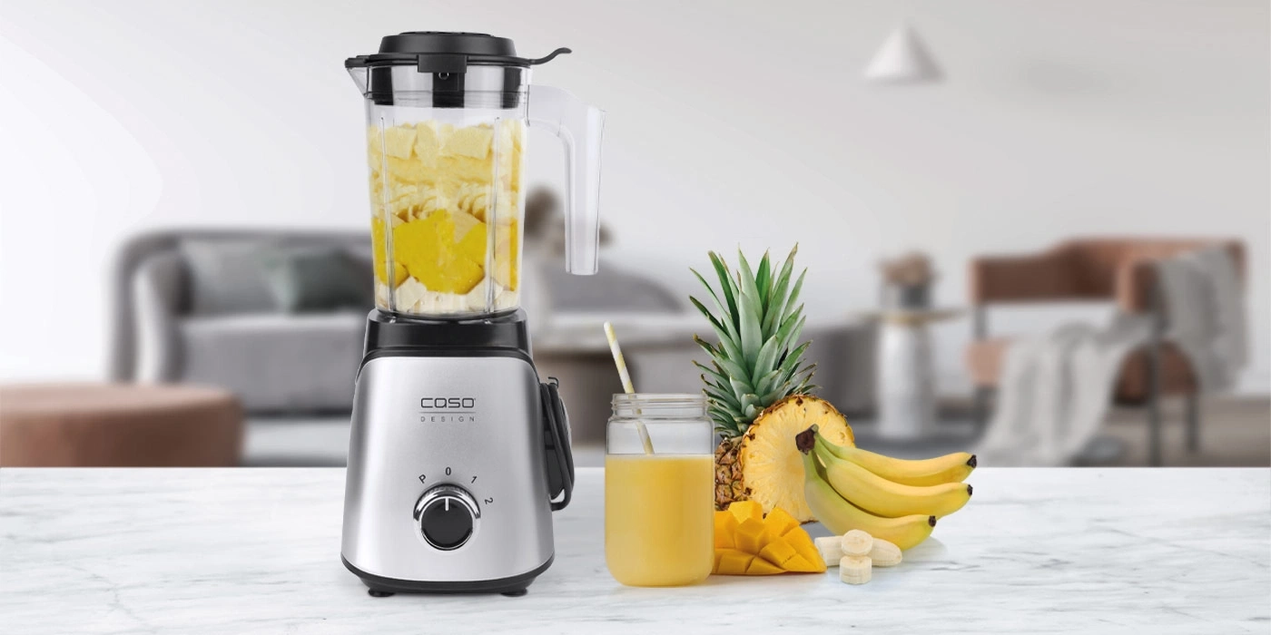 Blender with fruits and juice on a table in a bright room