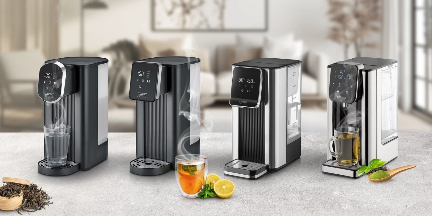 Vier Wasserspender mit digitalen Displays und Dampf, daneben Gläser mit Wasser und Tee.