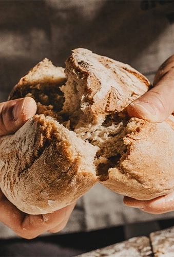 Nahaufnahme von Händen, die ein Brot zerreißen, das in zwei Hälften geteilt wird