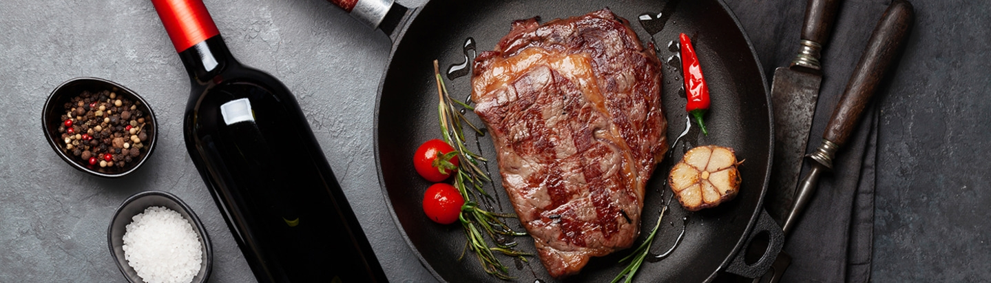 Gebratenes Steak mit Wein, Gewürzen und Küchenutensilien auf einem Tisch