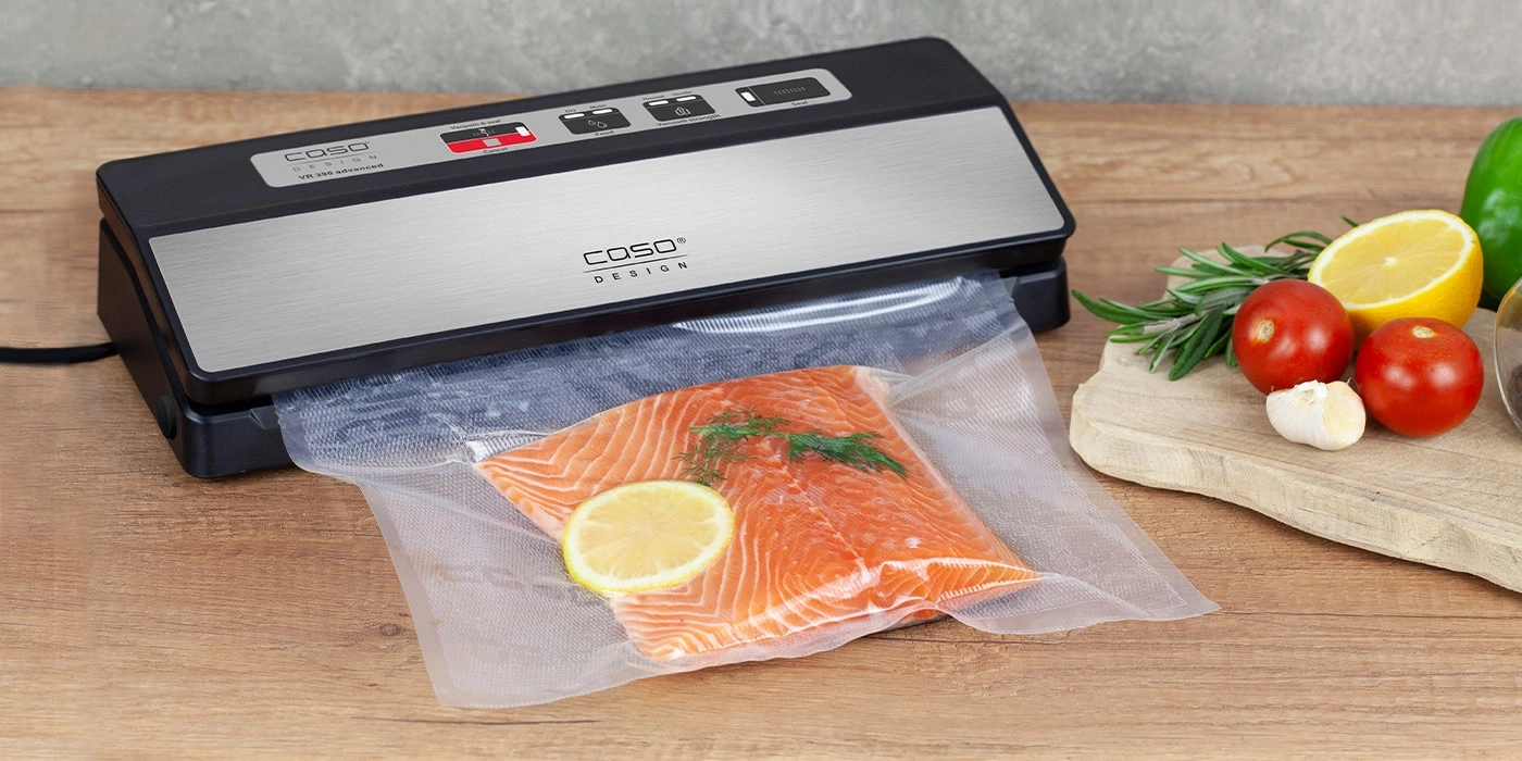 Vakuumiergerät mit Lachs, Zitrone und Gemüse auf Holzbrett