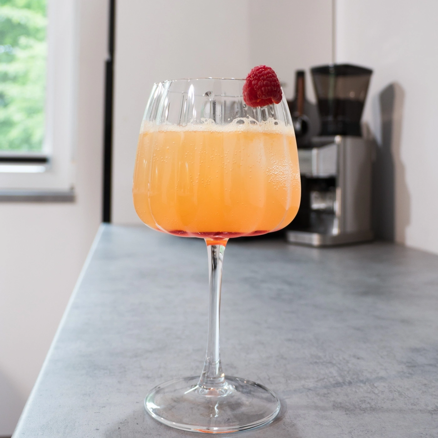 A glass of cocktail with raspberry on a kitchen counter.