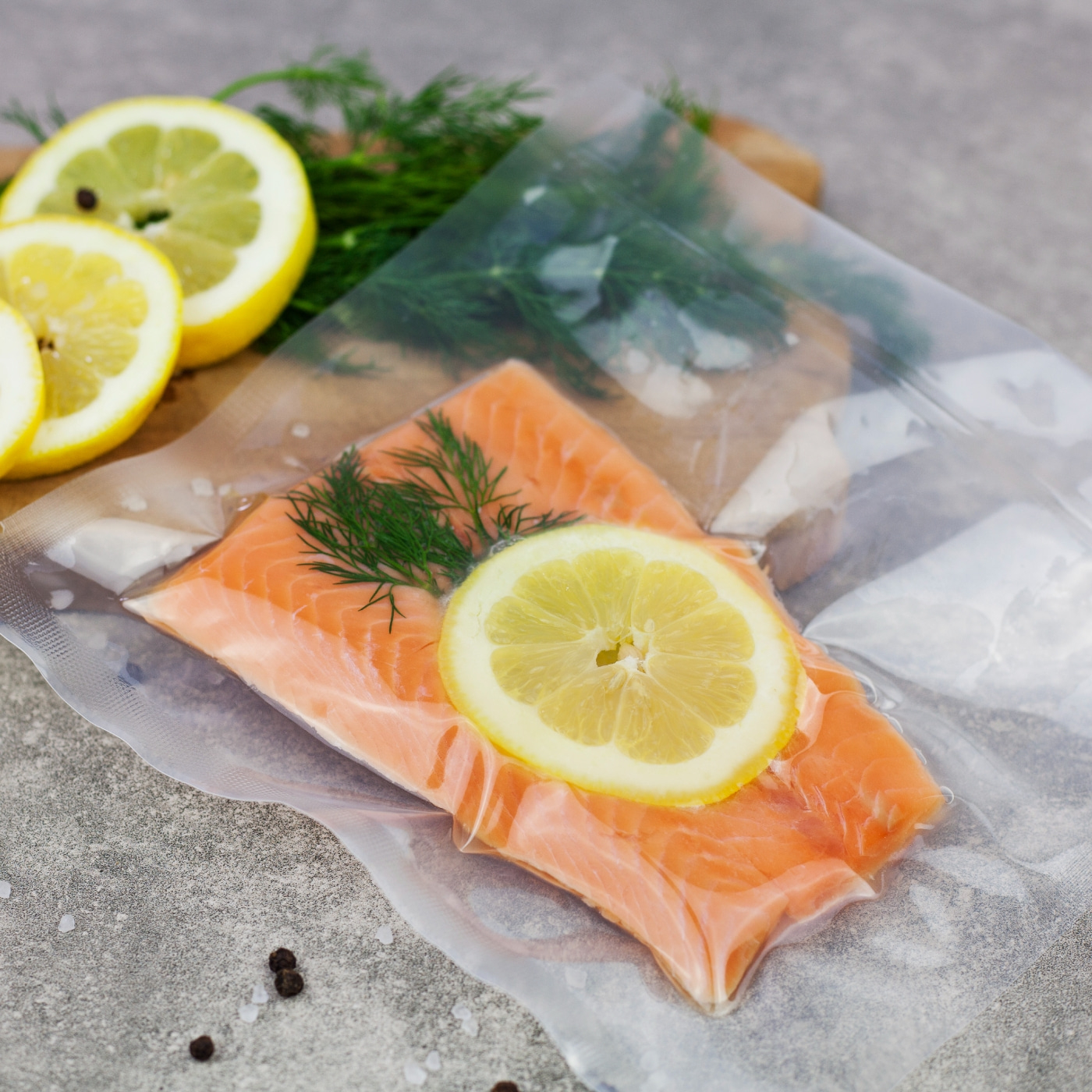 Salmon fillet with lemon and dill in vacuum packaging on a gray surface