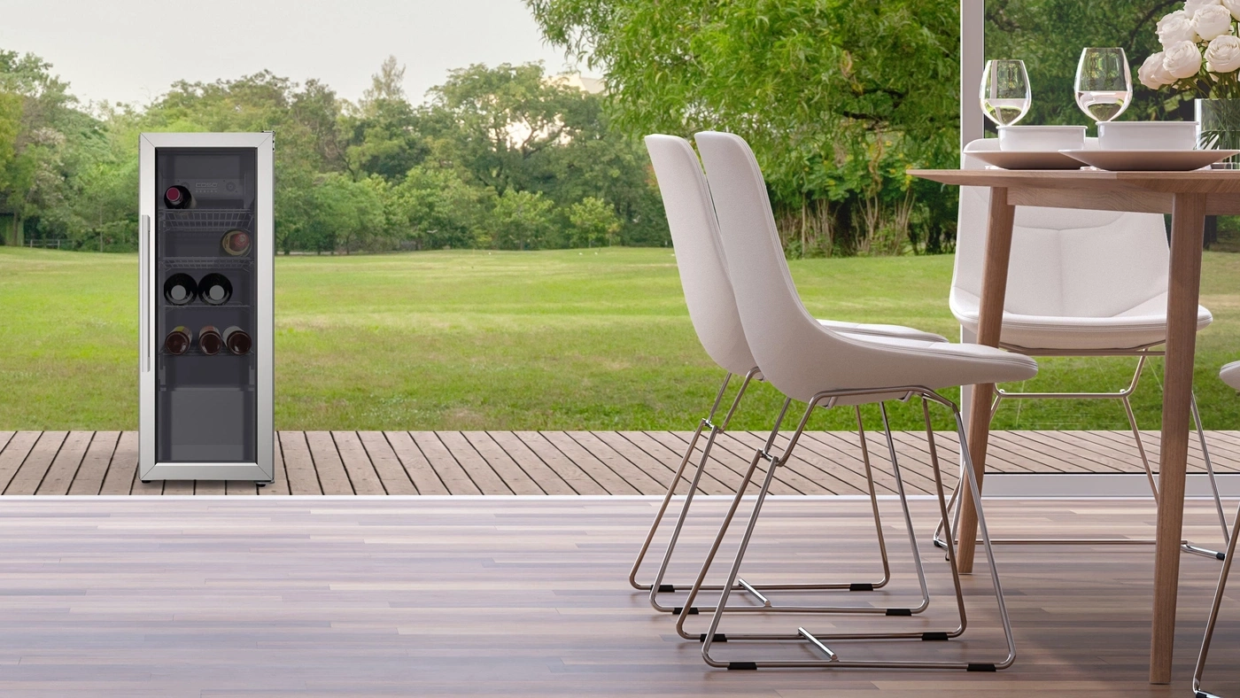 Wine cooler, chairs, and table on a patio overlooking a green lawn and trees.