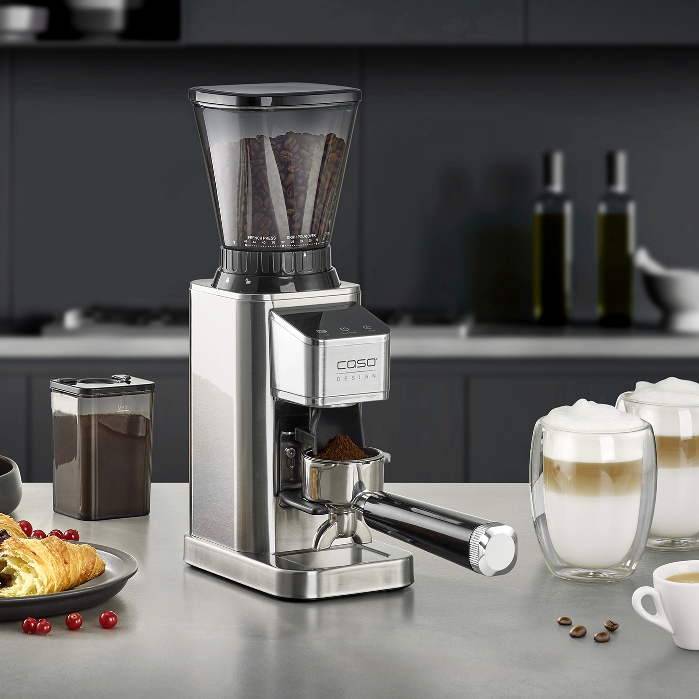 Kaffeemühle mit Zubehör, Kaffee und Gebäck auf einer Theke in einer Küche.