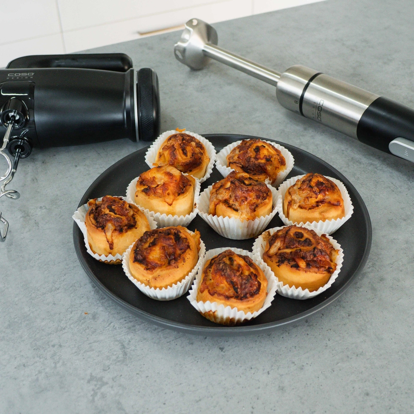 Plate of pastries, a mixer and a stick blender on a gray surface next to it.