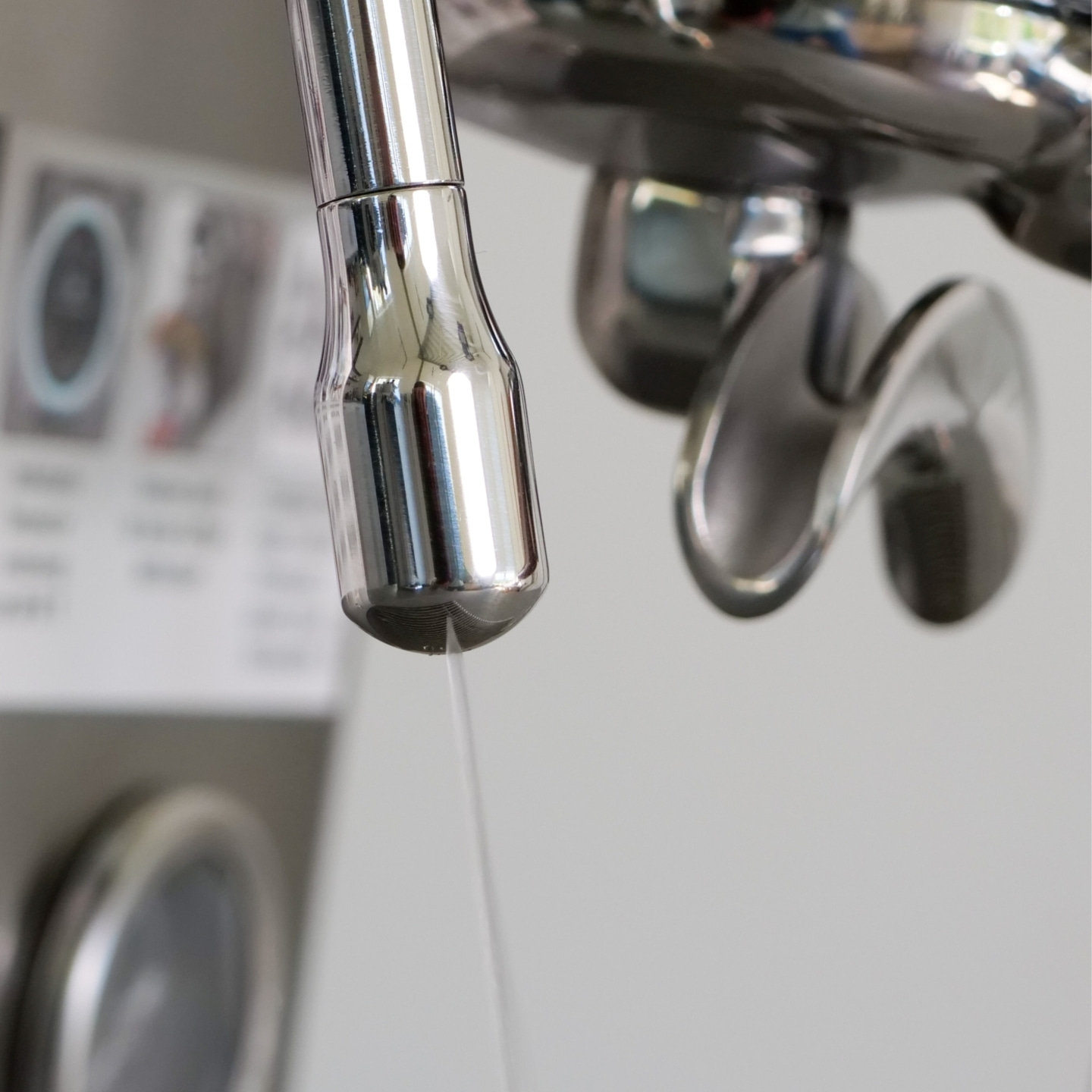 Close-up of water dripping from a chrome faucet with a blurred background of laundry machines.