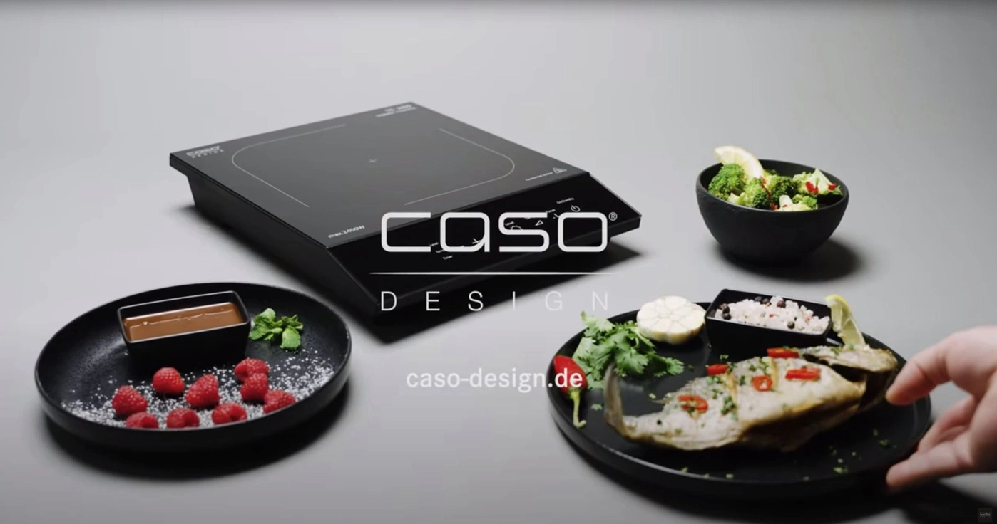 Induction cooktop with food, raspberries, broccoli and fish on black plate