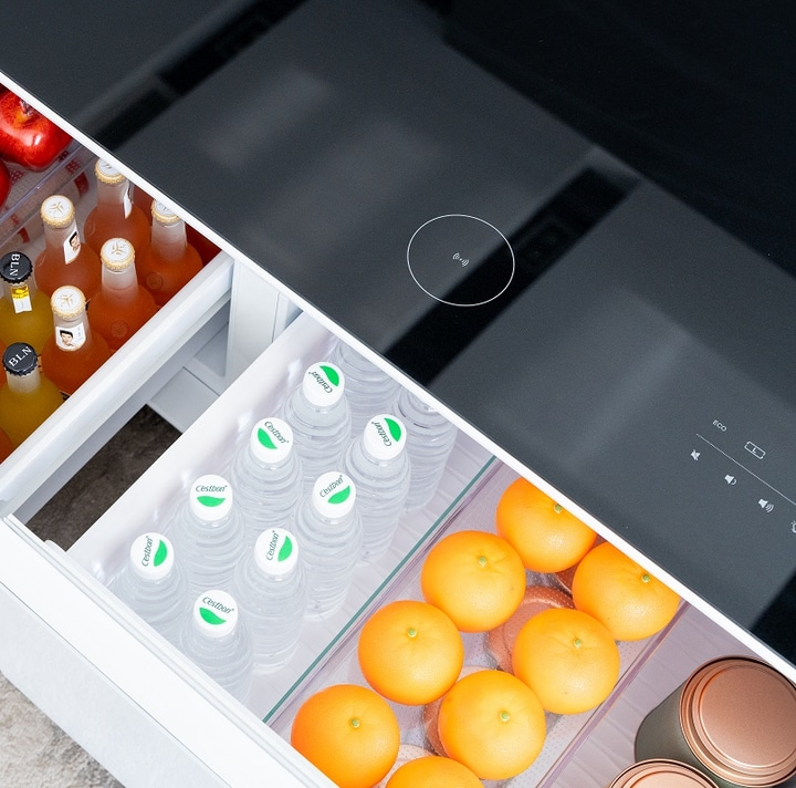 Kühlschrank mit Getränken und Obst, daneben eine schwarze Kochplatte mit Bedienfeld.