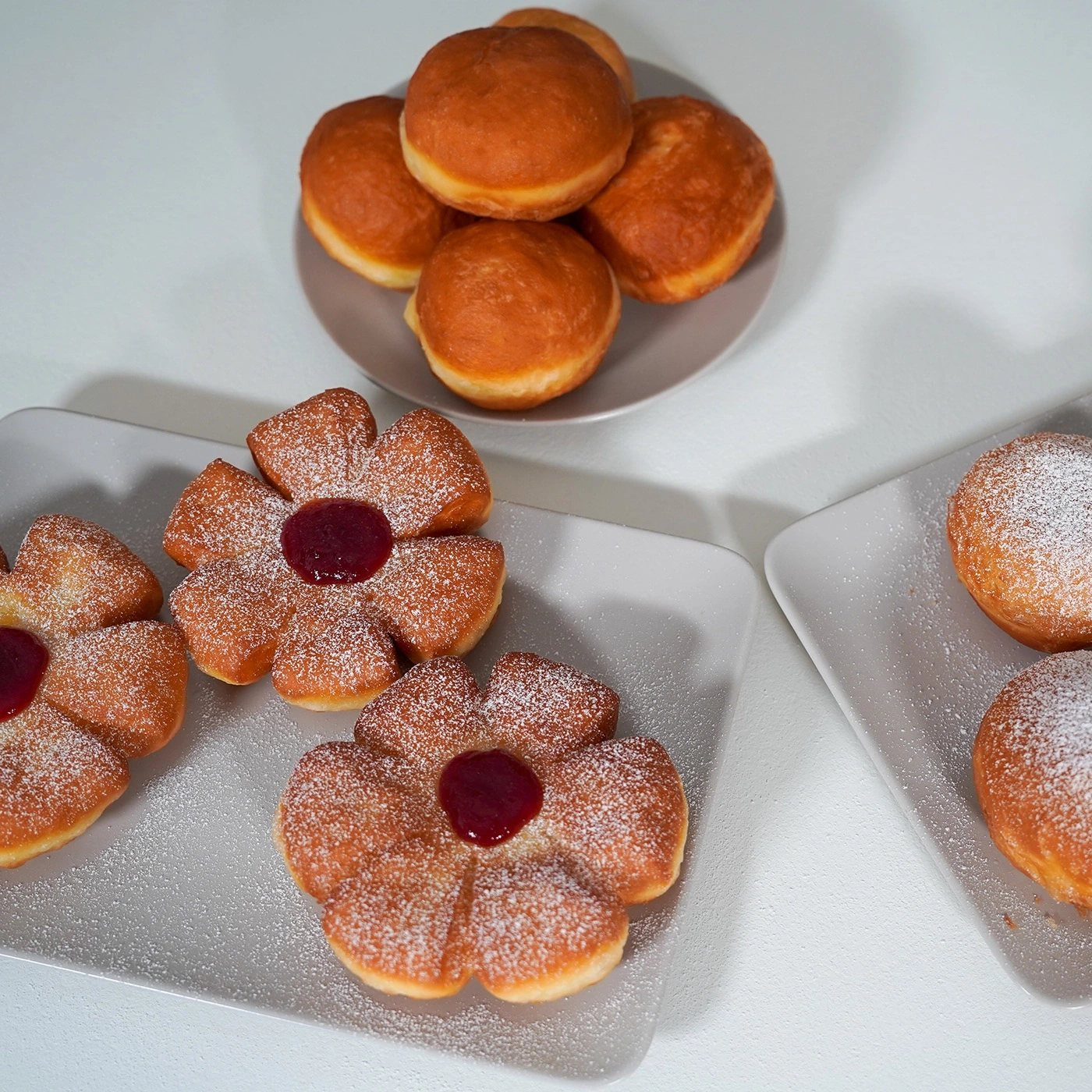 Blumenförmige und runde Donuts mit Puderzucker und Marmelade auf Tellern