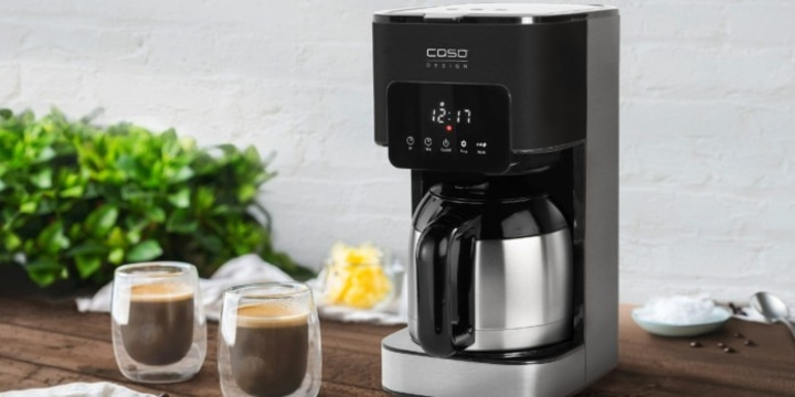 Coffee machine with two coffee glasses on a wooden table with greenery in the background.