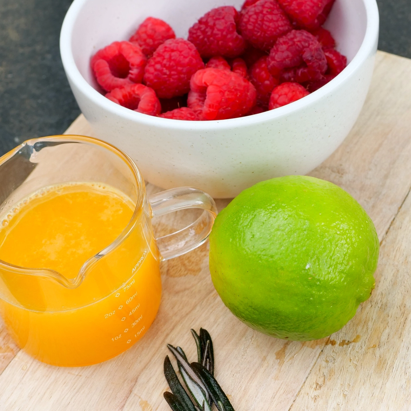 Fresh berries, lime, juice, and rosemary on a wooden board.