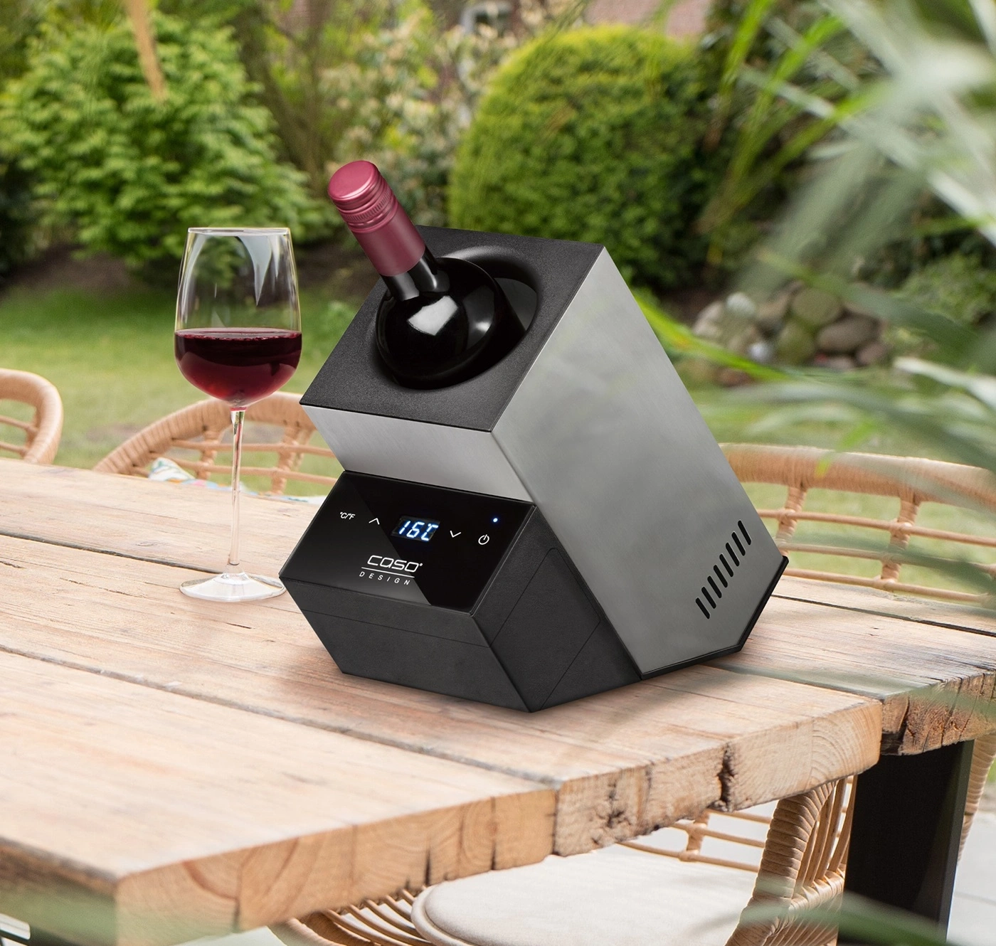 Weinkühler mit Wein und Glas auf Holztisch im Garten