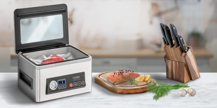 Vacuum sealer with meat, salmon, knife block, and garlic on a countertop.