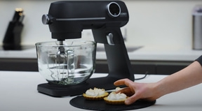 Kitchen mixer with pastries on a black plate, hand reaching for pastry