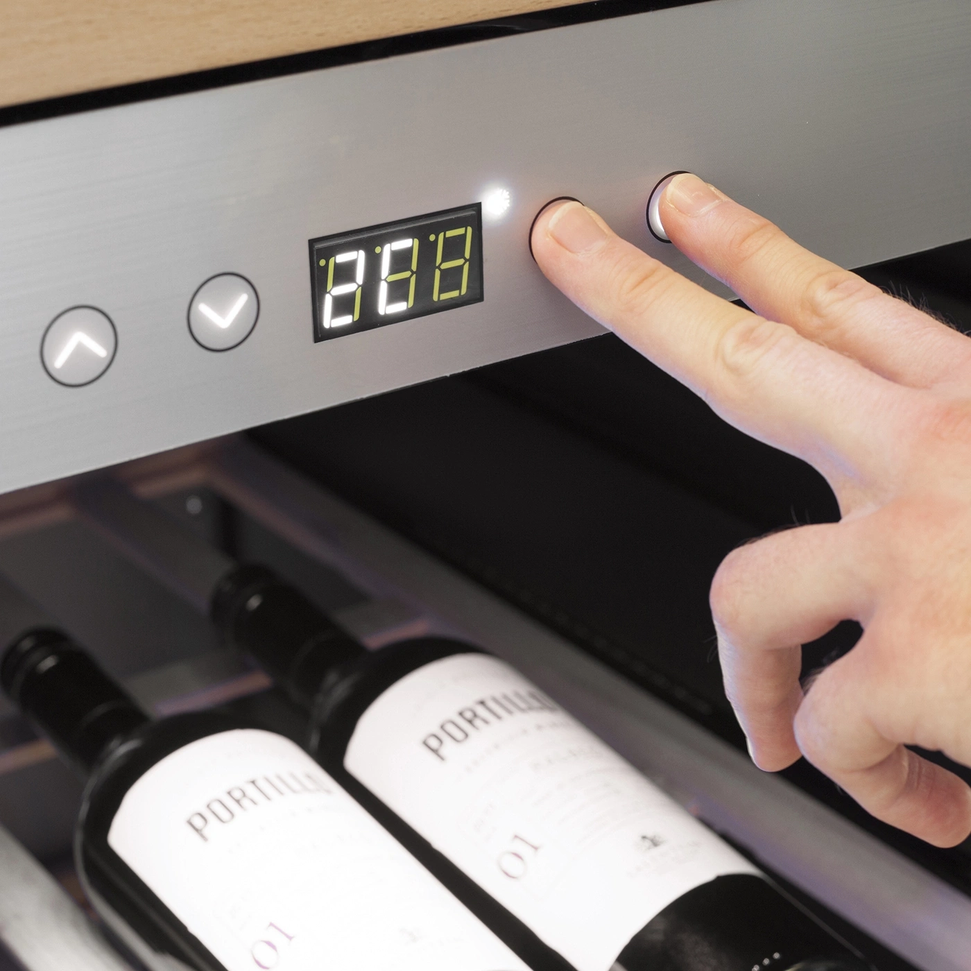 A man presses buttons on a wine cooler with two wine bottles.