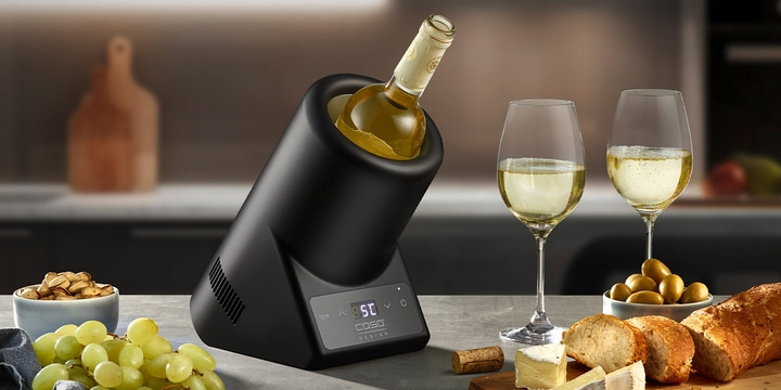 Wine cooler with wine, glasses, cheese, bread, and grapes on a table