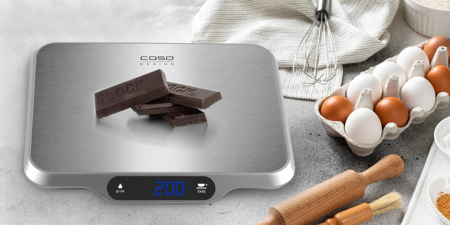 Scale with chocolate, eggs, and baking utensils on a gray surface