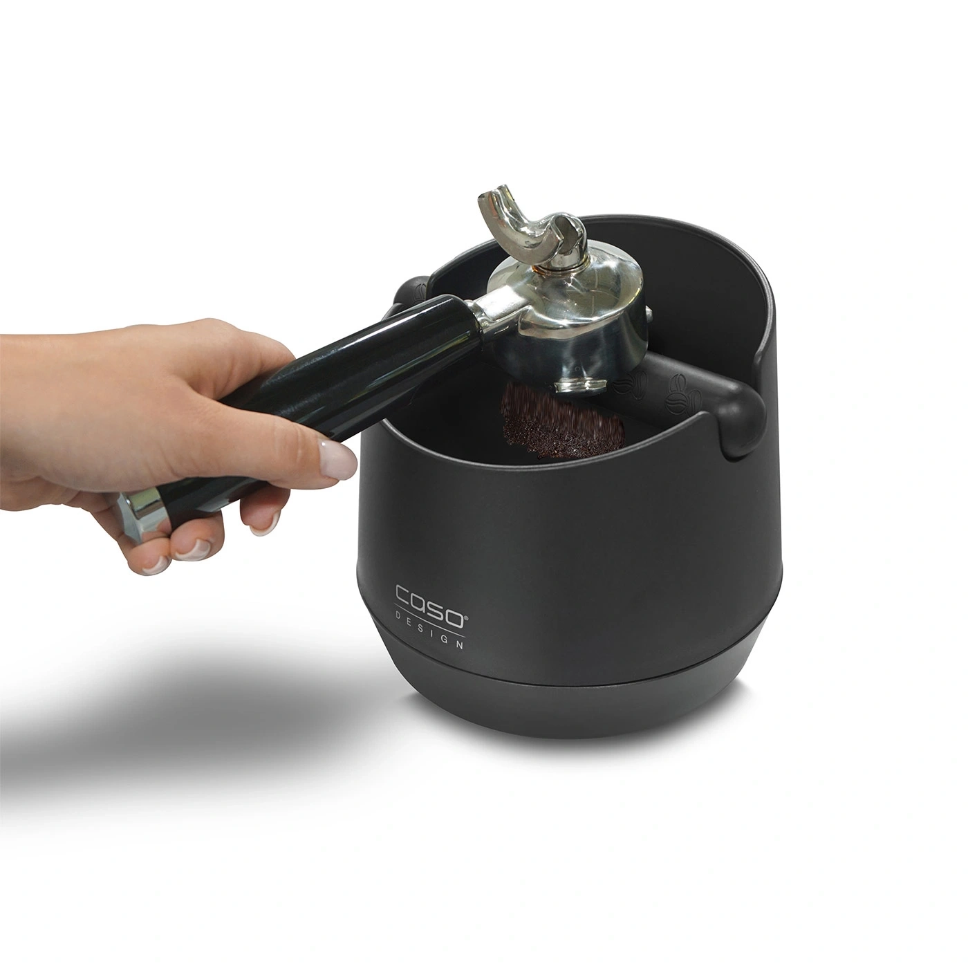 Person hält einen Siebträger über einem schwarzen Behälter mit Kaffeesatz.