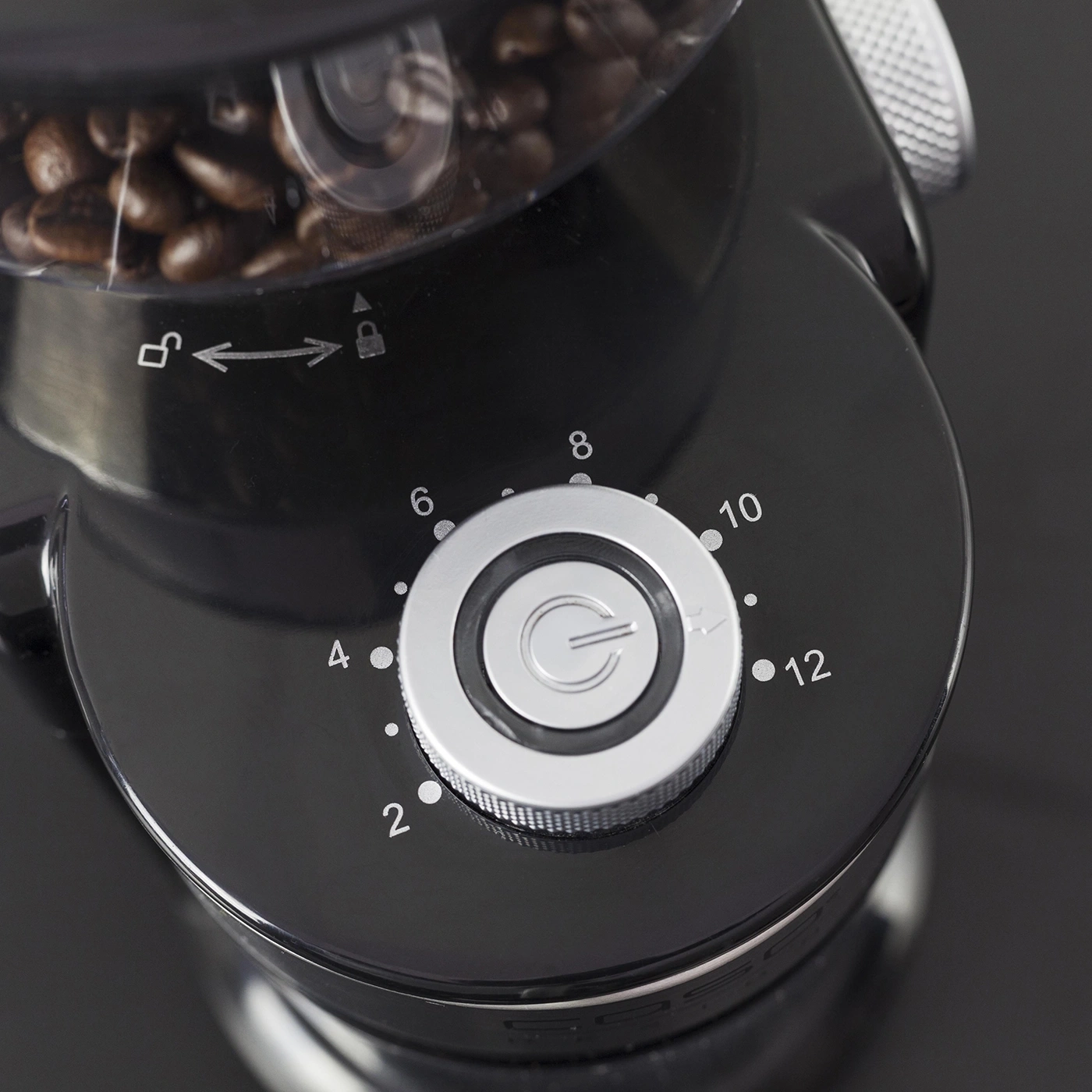 Close-up of a black coffee grinder with a dial and coffee beans in the container.