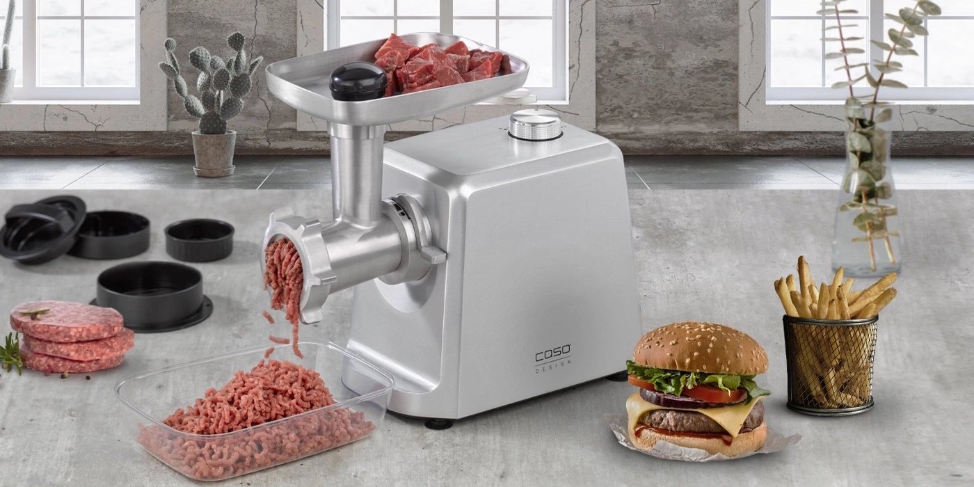 Fleischwolf mit Burger, Pommes und Zutaten auf einem Tisch.
