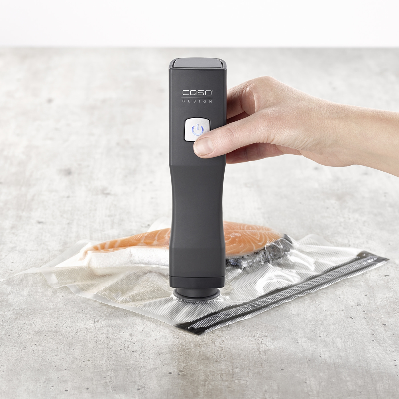 Vakuumiergerät mit Fisch in Plastikbeutel, Hand drückt Knopf, grauer Hintergrund.