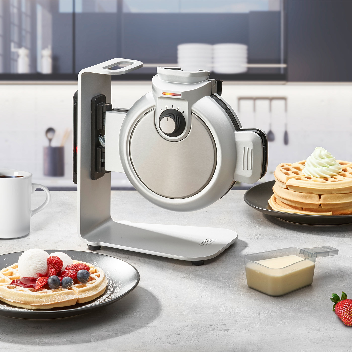 Waffle maker with waffles, ice cream, and berries on a kitchen table.