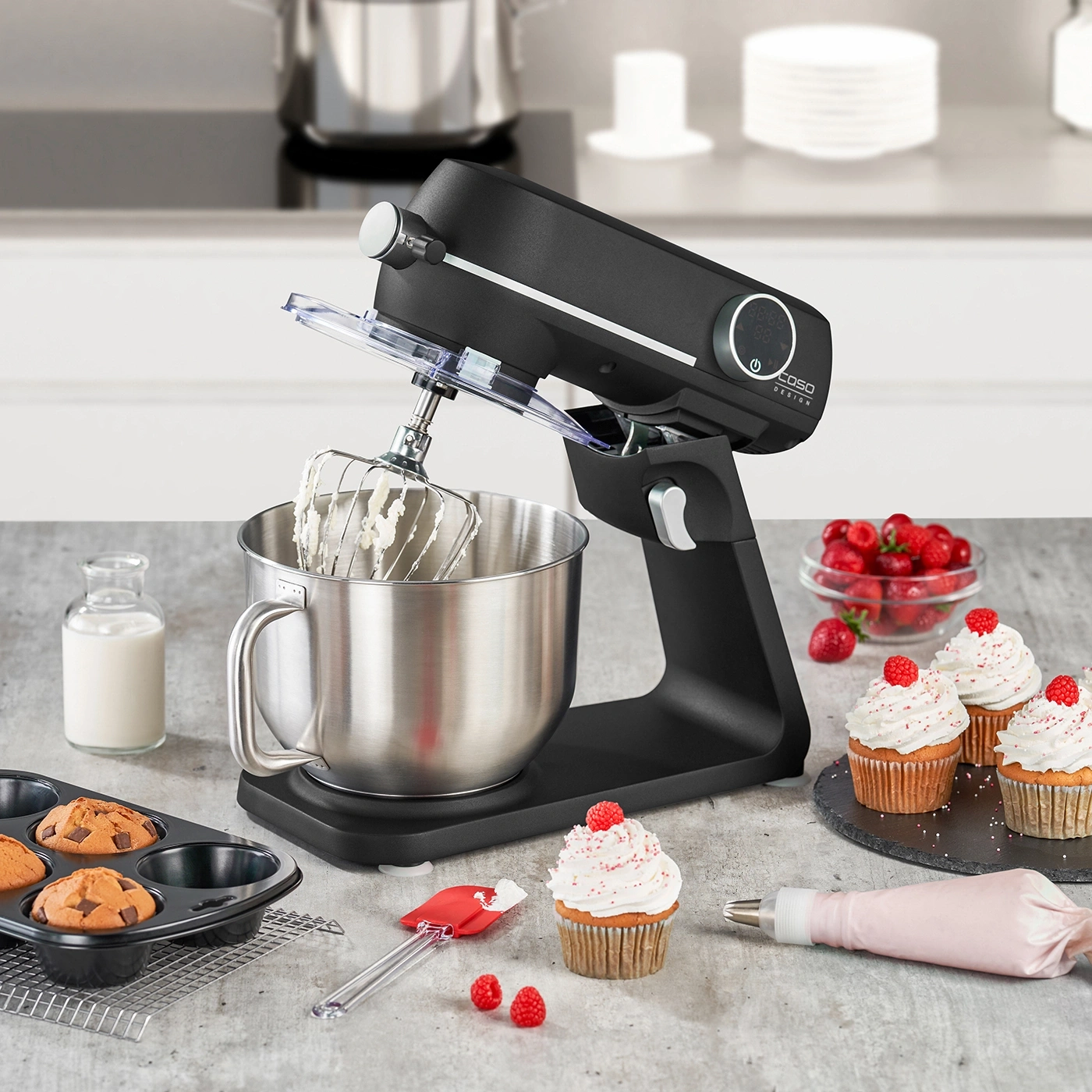 Stand mixer with cupcakes, raspberries, and baking utensils on a countertop