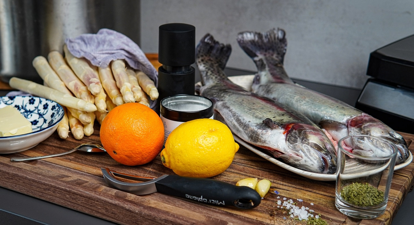 Two fish, asparagus, lemon, orange, garlic, butter, spices on wooden board