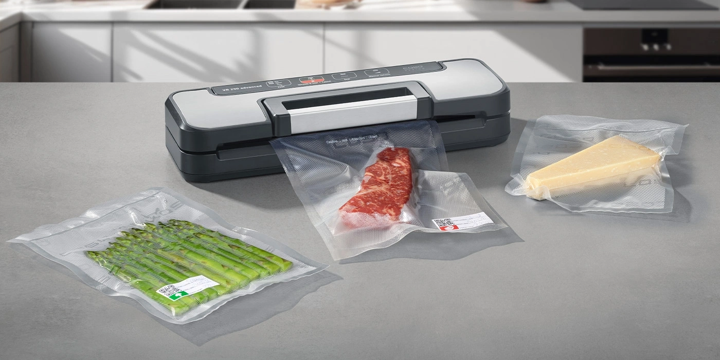 A vacuum sealer with meat, cheese, and asparagus on a countertop.
