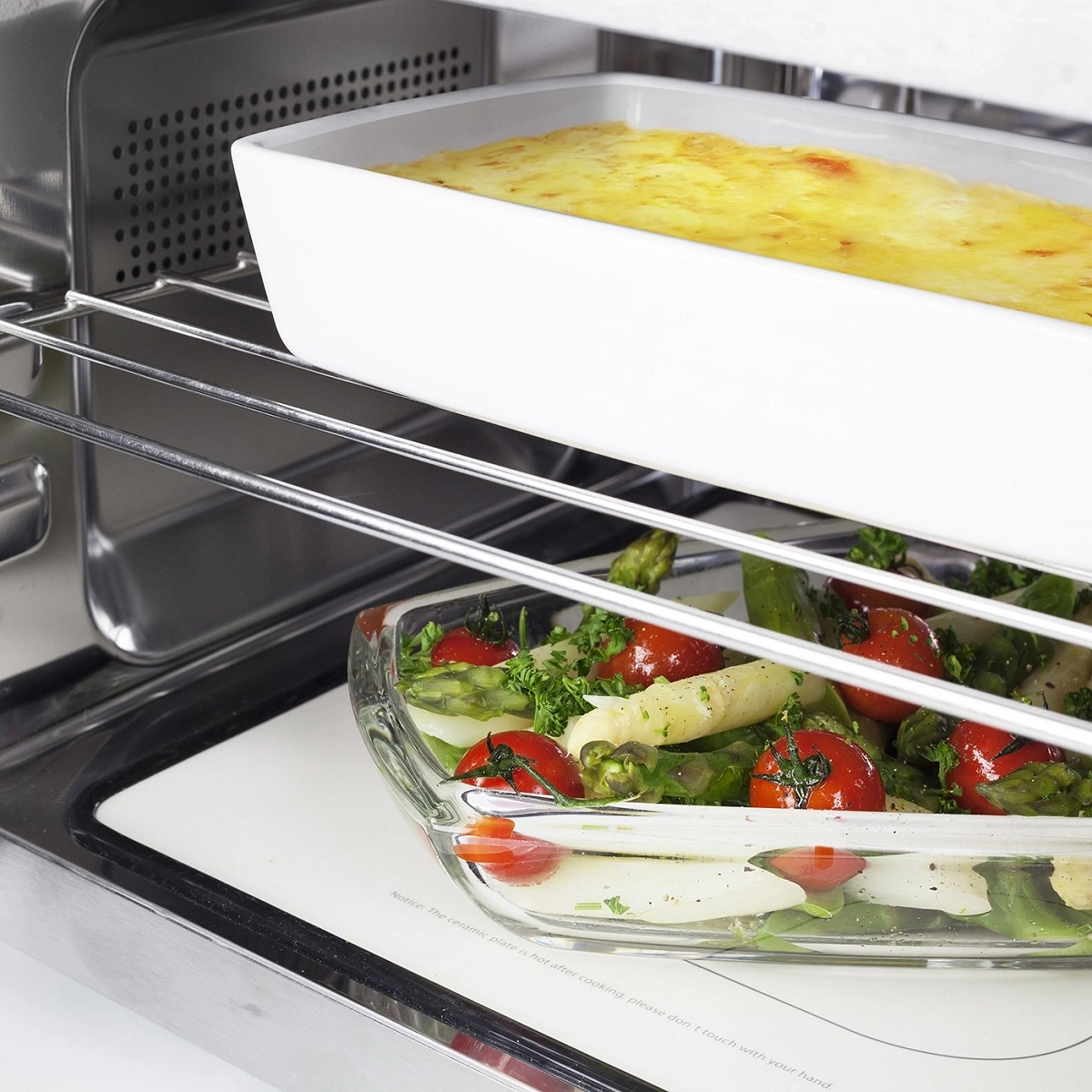 Oven with two dishes: casserole and vegetables. Warning: hot plate!