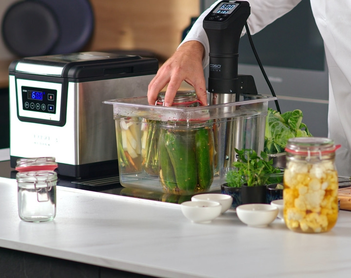 Sous-Vide-Gerät mit Gläsern und Gemüse auf einer weißen Arbeitsplatte