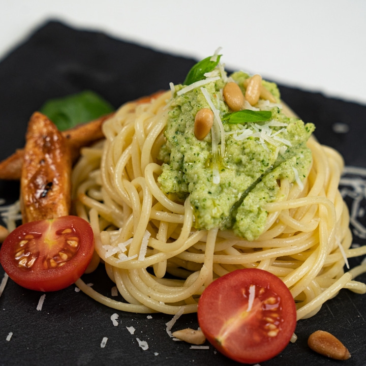Spaghetti with pesto, tomatoes, pine nuts, and cheese on a black plate