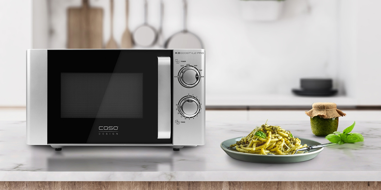 Microwave with food on a table. Pesto and pasta are visible in the image.