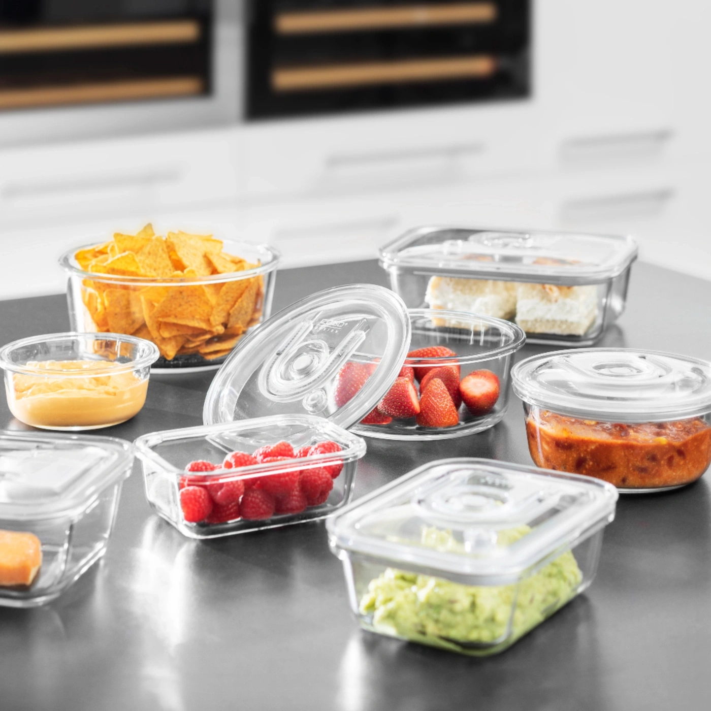 Glass containers with snacks like tortilla chips, strawberries, and guacamole on a tabletop