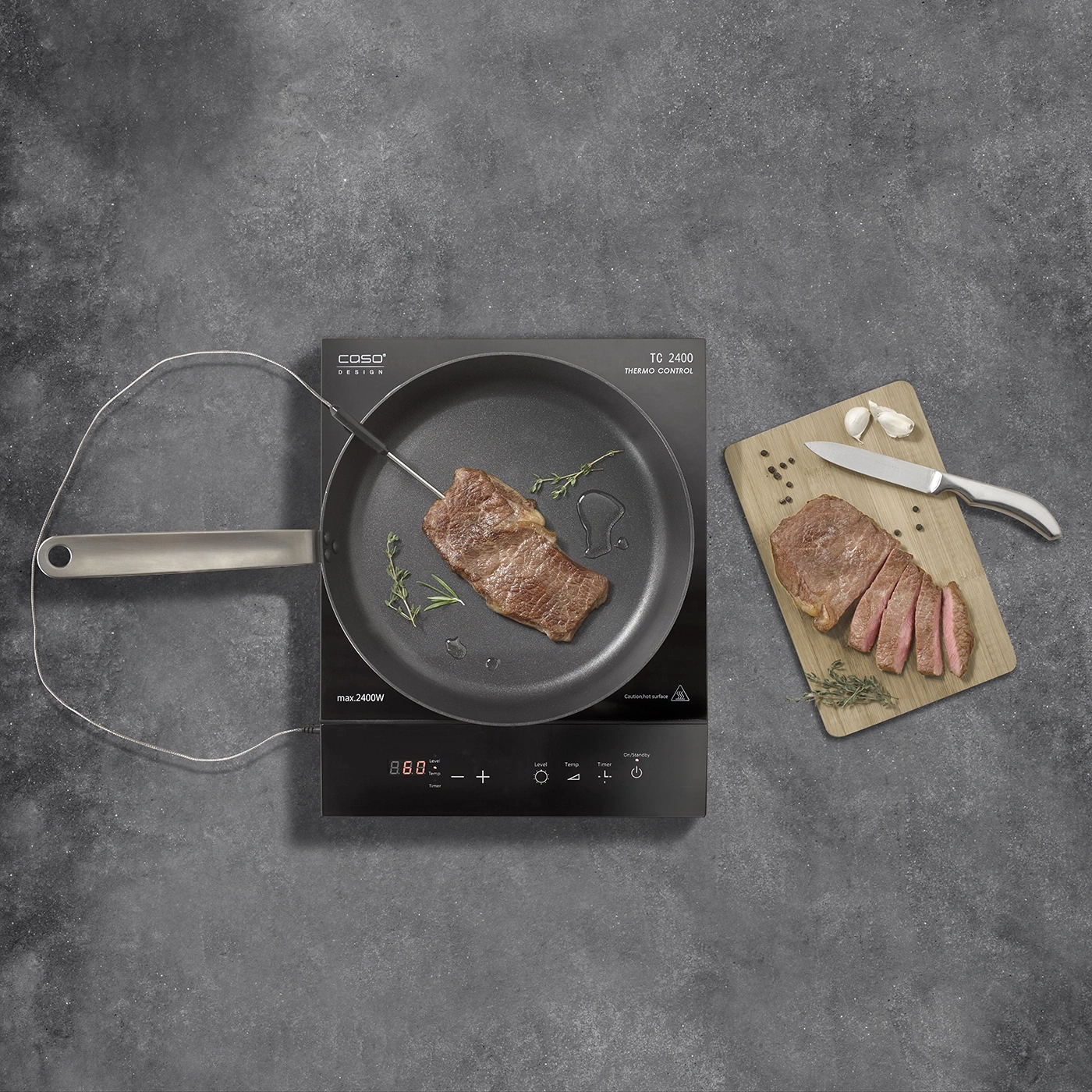 Steak cooking in pan, cutting board with sliced steak, garlic, and knife.