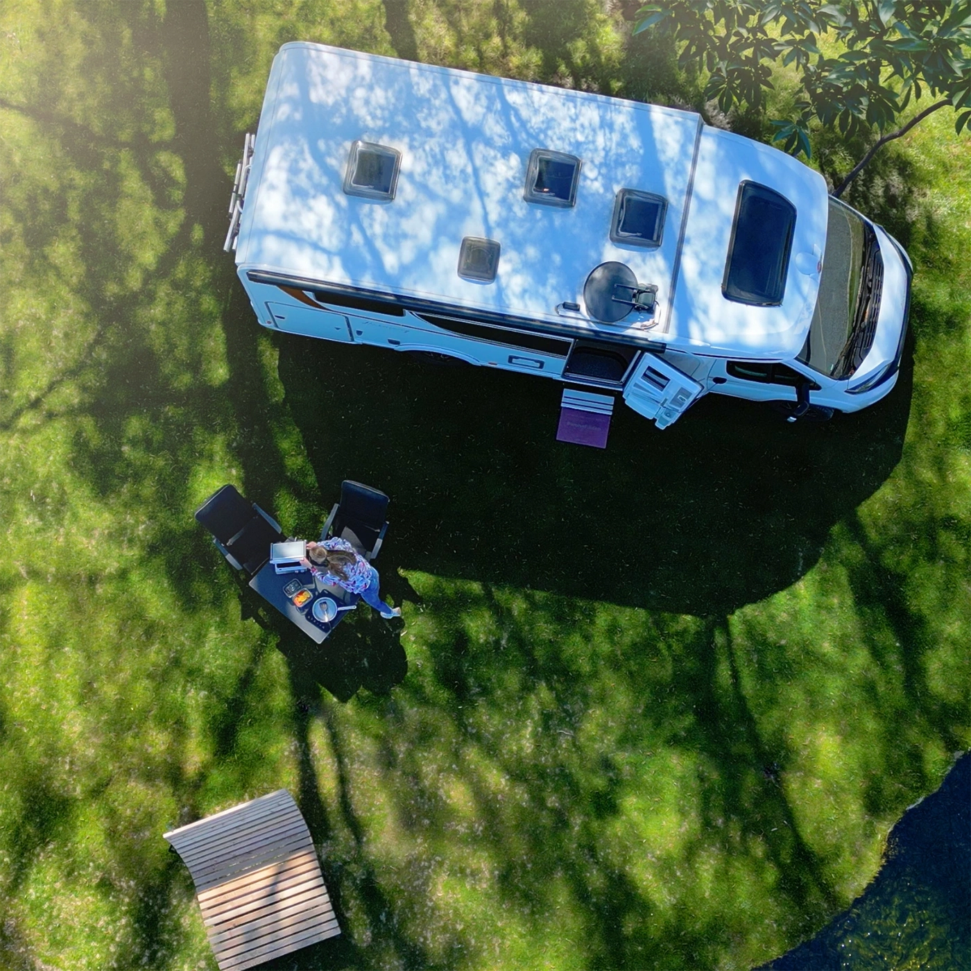 Eine Frau sitzt an einem Tisch im Gras neben einem Wohnmobil und arbeitet an ihrem Laptop.