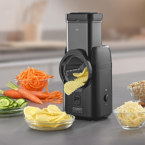 Electric vegetable slicer with vegetables and cheese in bowls on a gray surface.