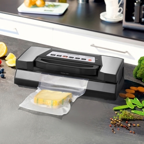 Vacuum sealer with cheese, vegetables, and spices on a kitchen countertop