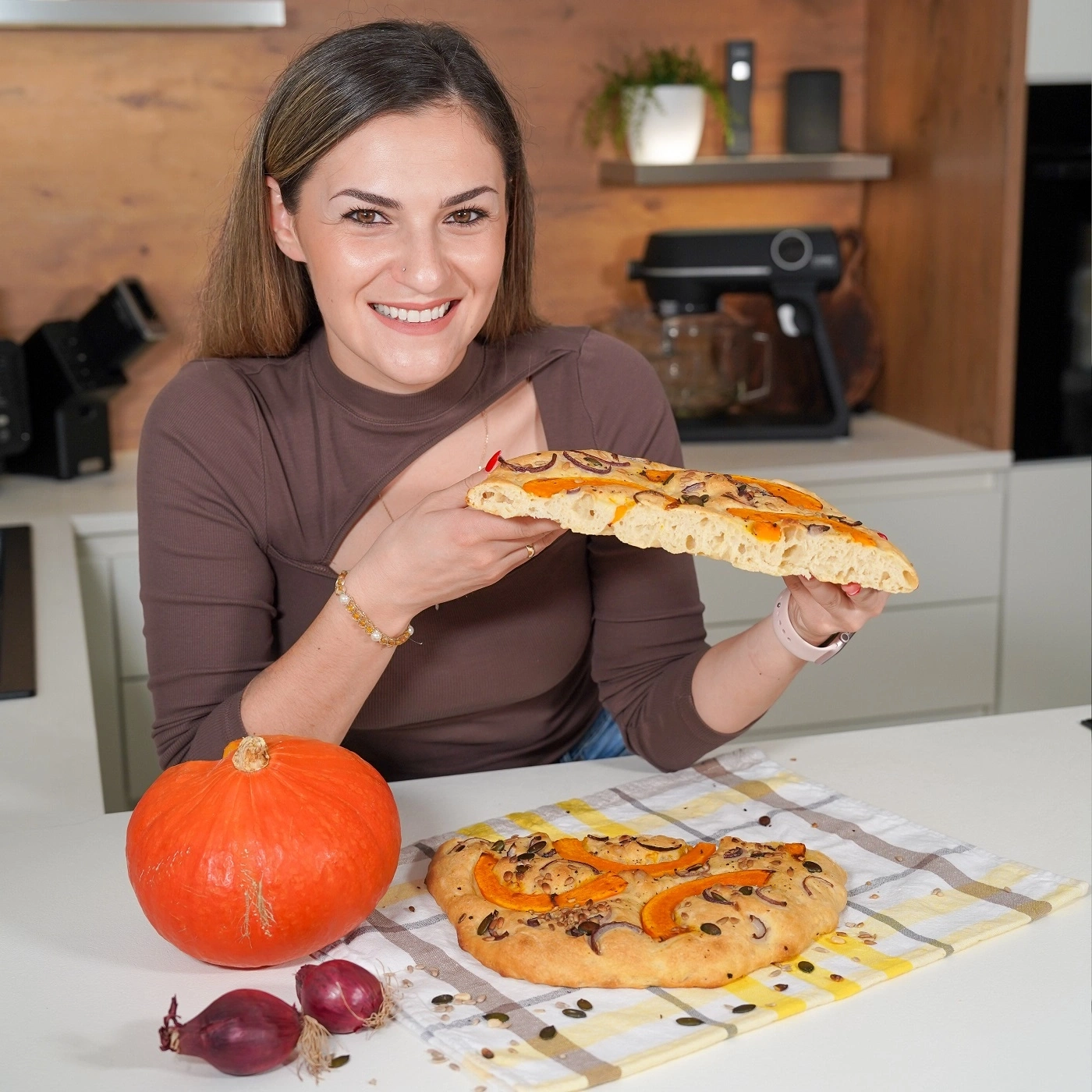 Woman holding bread with pumpkin and onions, smiling at the camera.