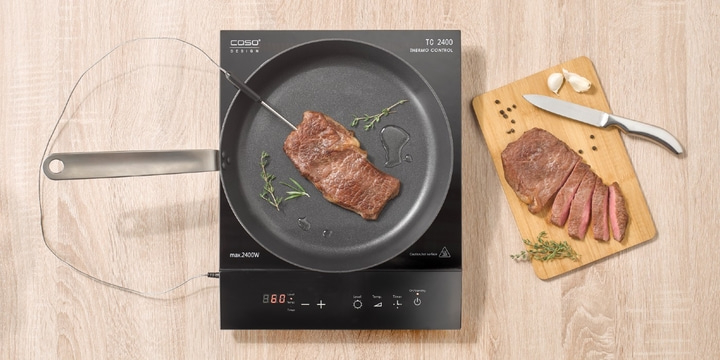 Cooked steak on cooktop with accessories and wooden board