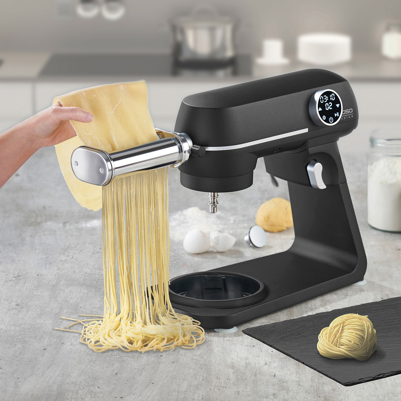 Pasta maker machine producing fresh spaghetti noodles in kitchen.