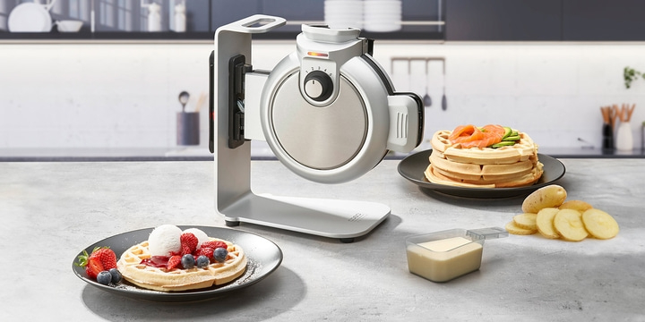Waffle iron with waffles, berries, salmon, and potatoes on a kitchen table setting.