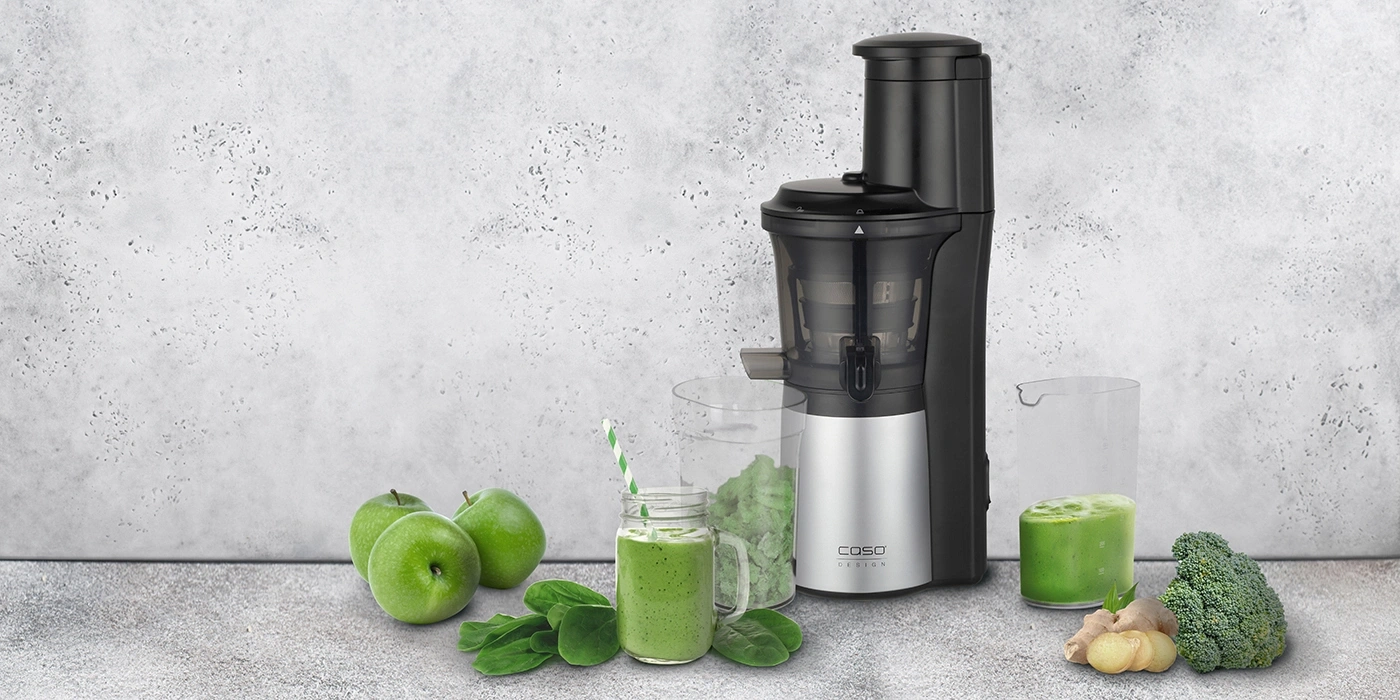 Grüner Smoothie mit Zutaten und Entsafter auf grauem Hintergrund