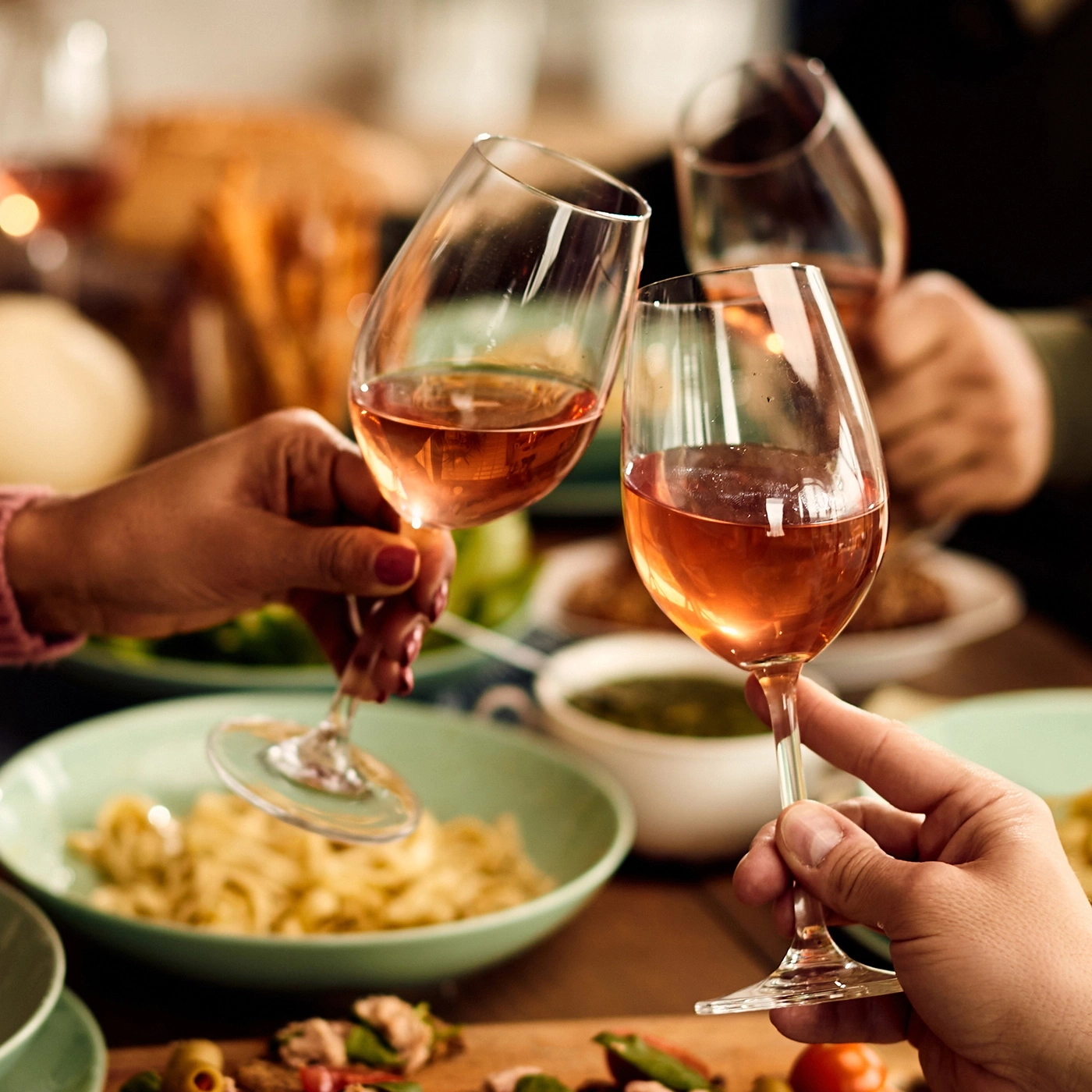 People toasting with rosé wine during a shared meal.