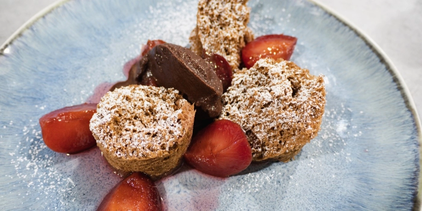 Schokoladenmousse mit Kuchenstücken und Erdbeeren auf blauem Teller.