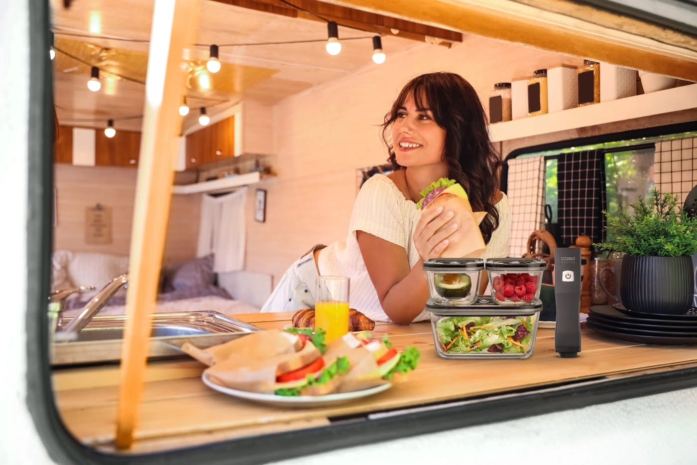 Frau in einem Wohnmobil, die ein Sandwich hält, mit Essen und Geräten.